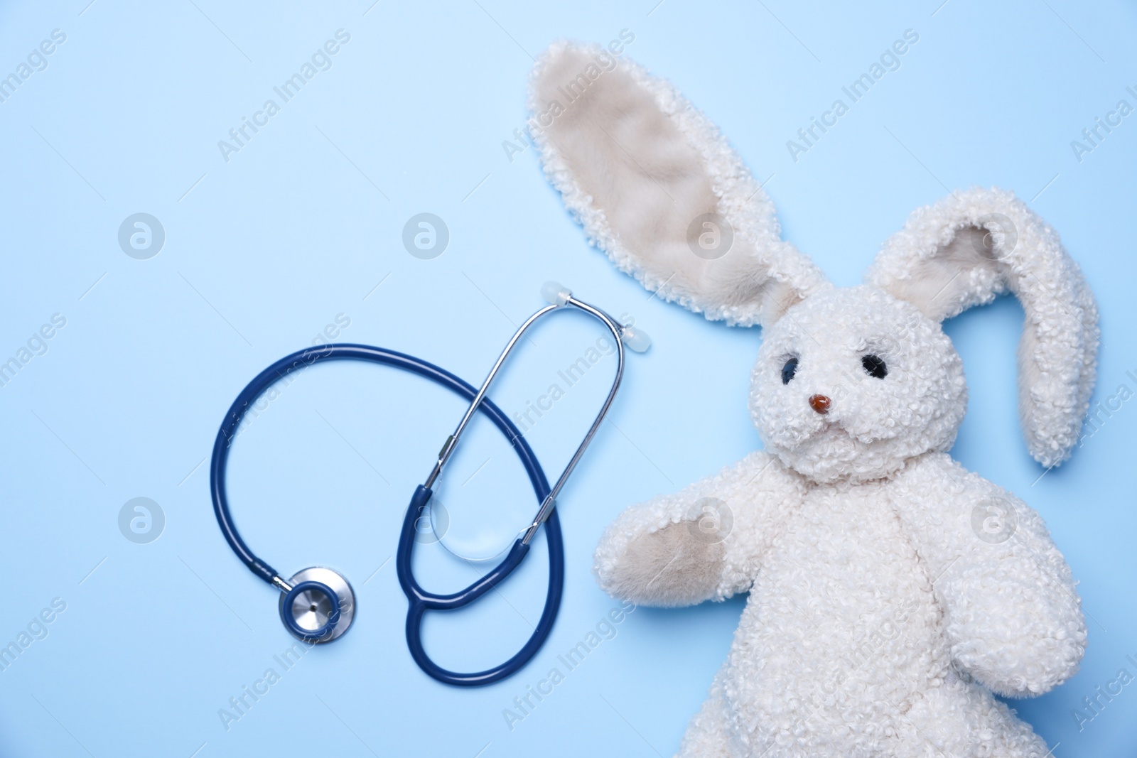 Photo of Pediatrics concept. Toy bunny with stethoscope on light blue background, top view. Space for text