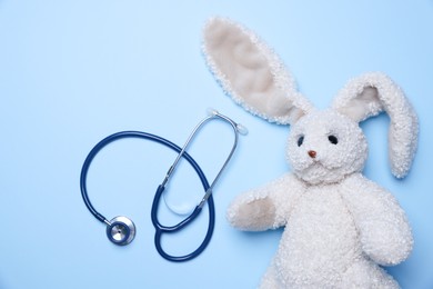 Photo of Pediatrics concept. Toy bunny with stethoscope on light blue background, top view. Space for text