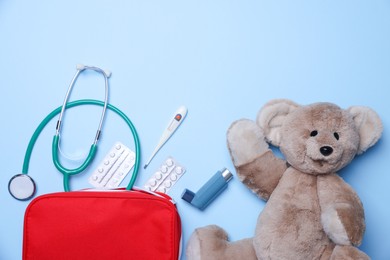 Photo of Pediatrics concept. Toy bear with stethoscope and first aid kit on light blue background, flat lay