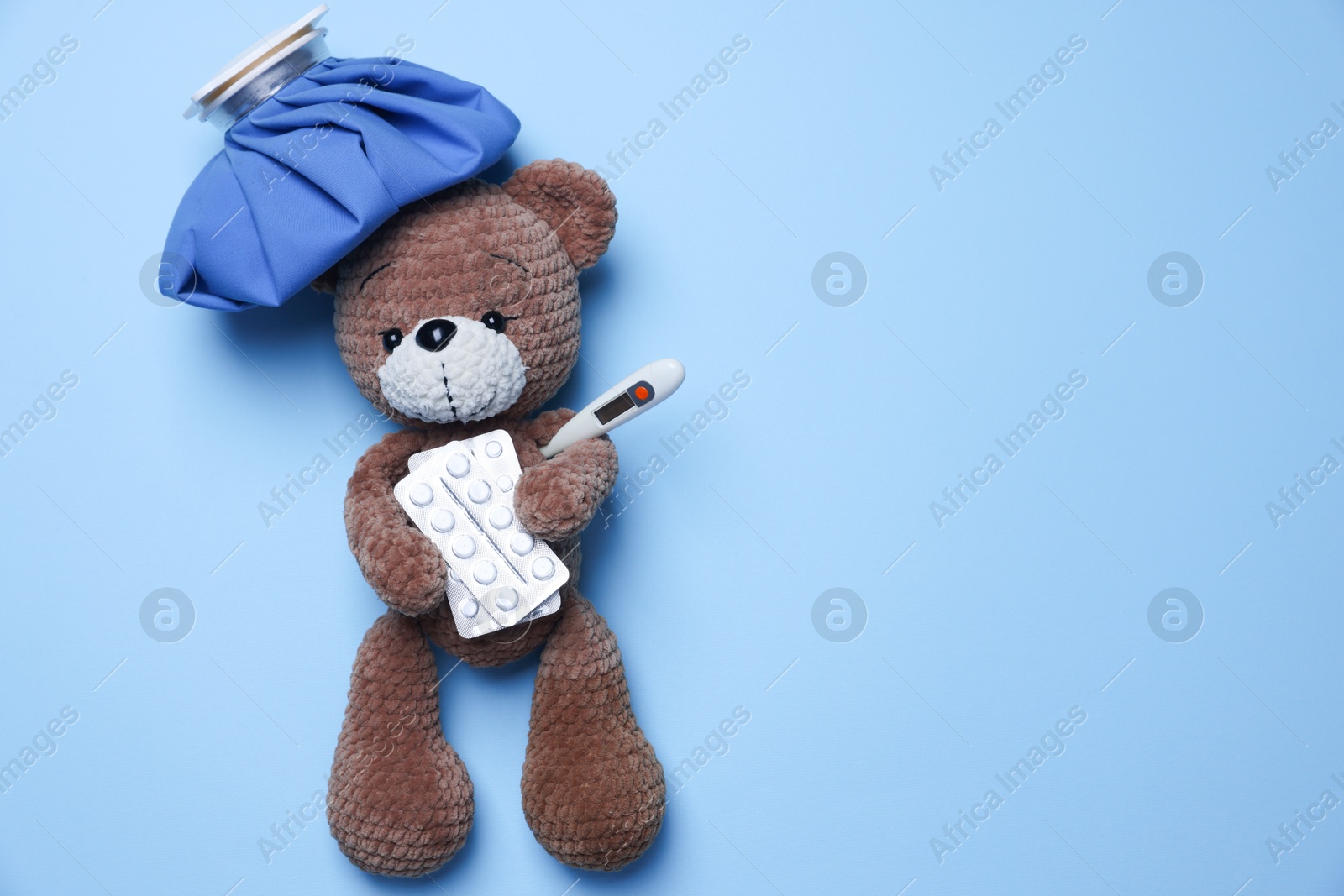 Photo of Pediatrics concept. Toy bear with ice bag, pills and thermometer on light blue background, top view. Space for text