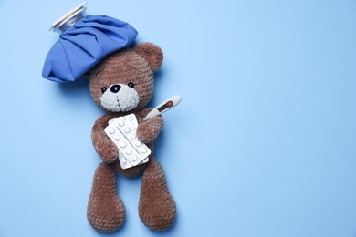 Photo of Pediatrics concept. Toy bear with ice bag, pills and thermometer on light blue background, top view. Space for text