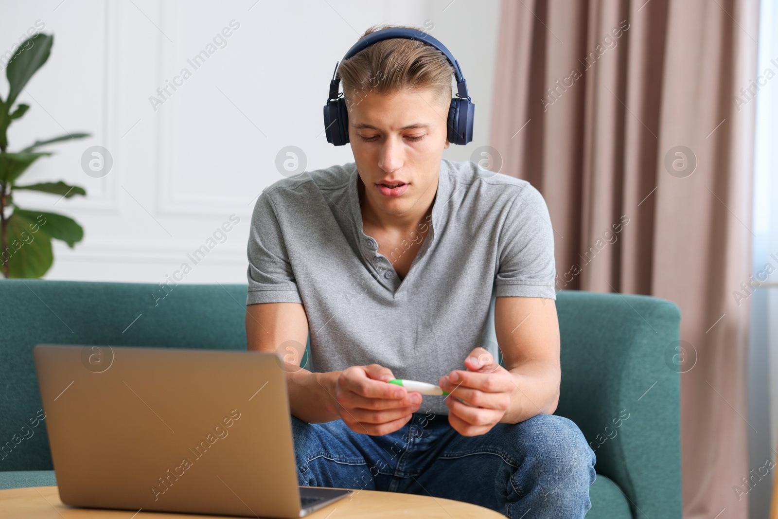 Man in headphones with thermometer having online consultation with doctor via laptop at home Photo of Man in headphones with thermometer having online consultation with doctor via laptop at home