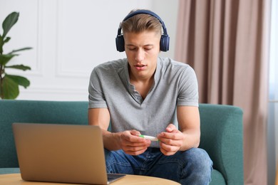 Photo of Man in headphones with thermometer having online consultation with doctor via laptop at home