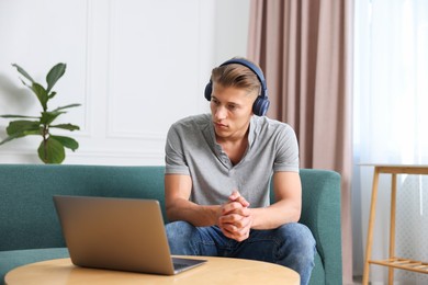 Photo of Man in headphones having online consultation with doctor via laptop at home