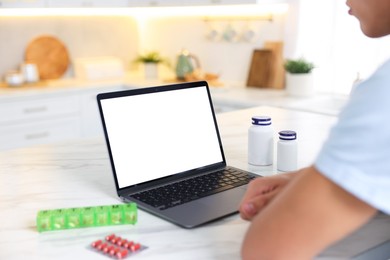 Photo of Man having online consultation with doctor via laptop at table in kitchen, closeup
