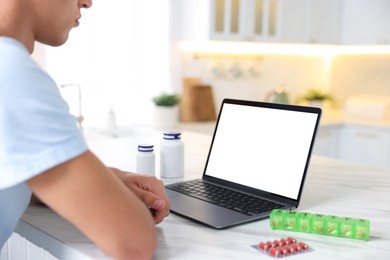 Photo of Man having online consultation with doctor via laptop at table in kitchen, closeup
