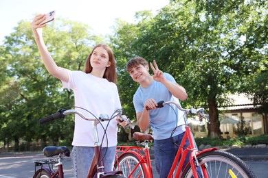 Photo of Teenage girl and boy with bicycles taking selfie on city street