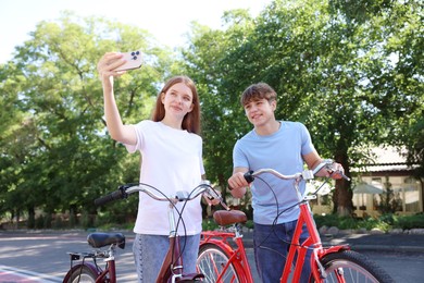 Photo of Teenage girl and boy with bicycles taking selfie on city street