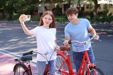 Photo of Teenage girl and boy with bicycles taking selfie on city street