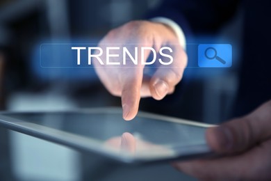 Image of Businessman using tablet computer to find hot tendencies, new ideas, popular directions, closeup. Search bar with word Trends