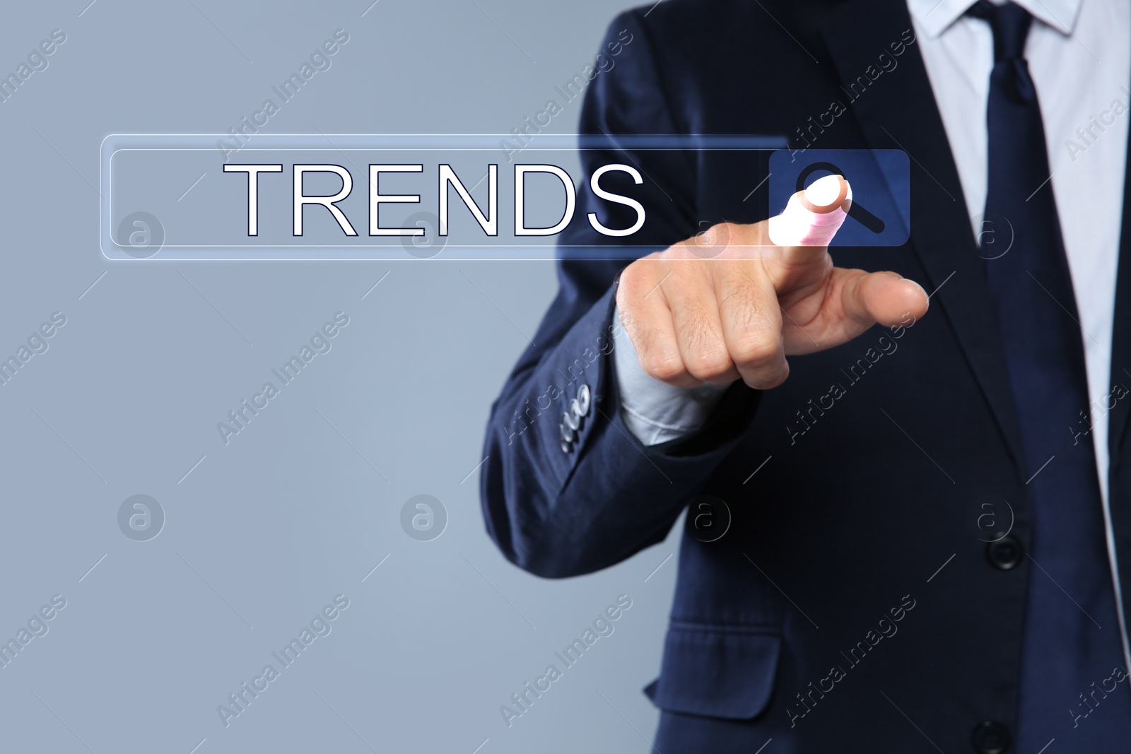 Image of Businessman using virtual screen to find hot tendencies, new ideas, popular directions against grey background, closeup. Search bar with word Trends