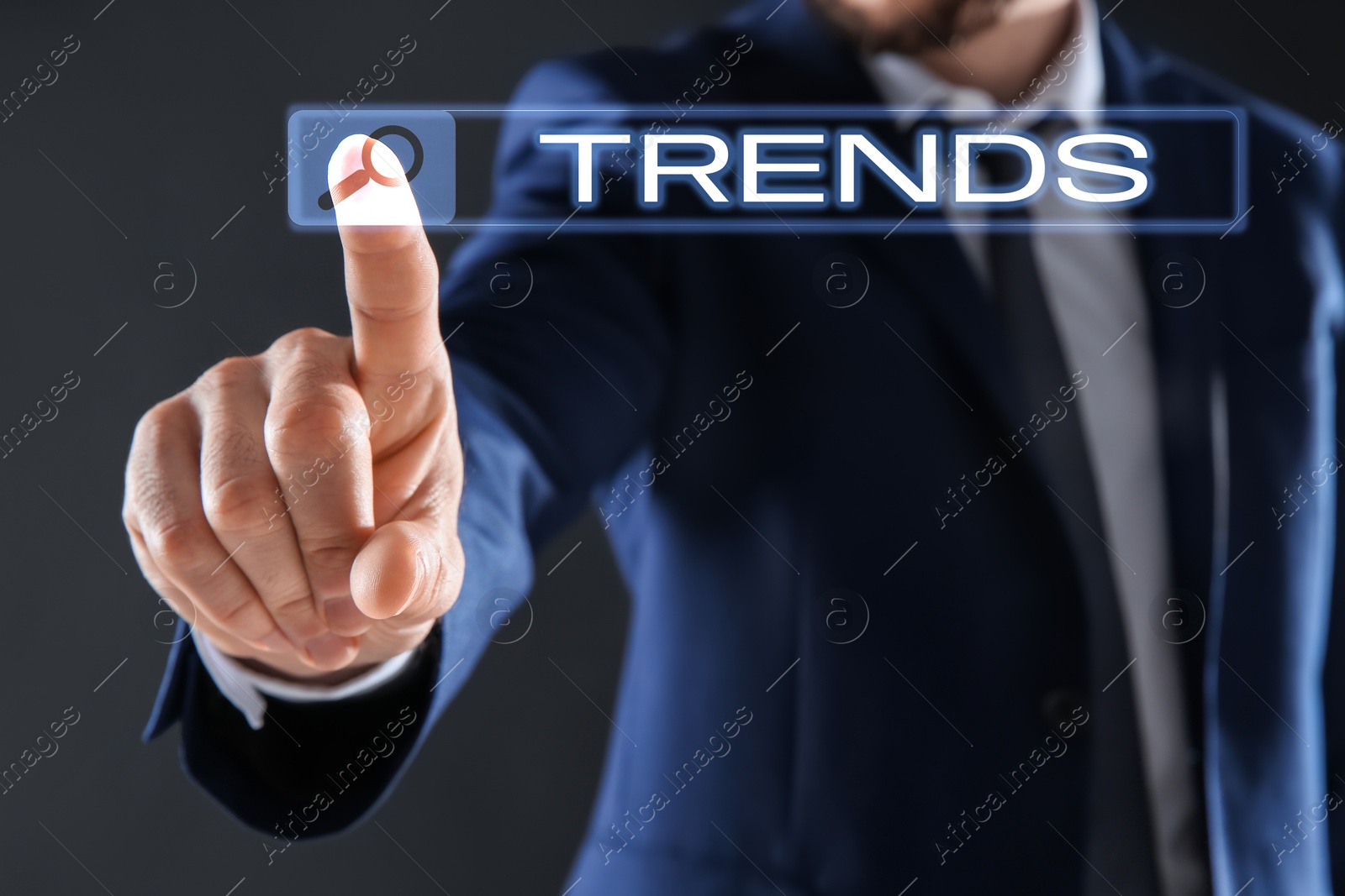 Image of Businessman using virtual screen to find hot tendencies, new ideas, popular directions against grey background, closeup. Search bar with word Trends