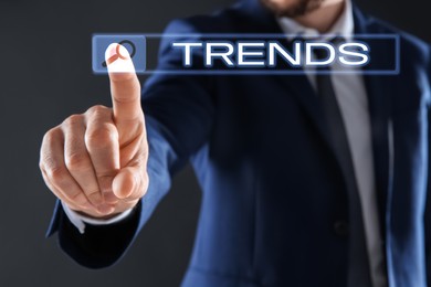 Image of Businessman using virtual screen to find hot tendencies, new ideas, popular directions against grey background, closeup. Search bar with word Trends