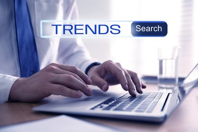 Image of Businessman using laptop to find hot tendencies, new ideas, popular directions at table, closeup. Search bar with word Trends