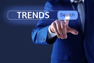 Image of Businessman using virtual screen to find hot tendencies, new ideas, popular directions against dark blue background, closeup. Search bar with word Trends