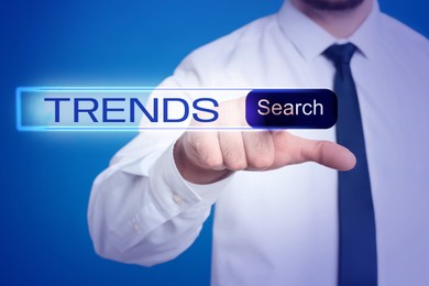 Image of Businessman using virtual screen to find hot tendencies, new ideas, popular directions against blue background, closeup. Search bar with word Trends