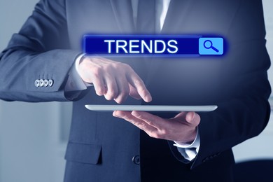 Image of Businessman using tablet computer to find hot tendencies, new ideas, popular directions, closeup. Search bar with word Trends