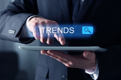 Image of Businessman using tablet computer to find hot tendencies, new ideas, popular directions, closeup. Search bar with word Trends