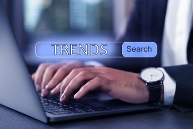 Image of Businessman using laptop to find hot tendencies, new ideas, popular directions at table, closeup. Search bar with word Trends