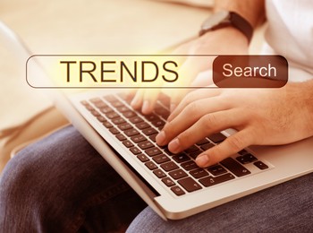 Image of Man using laptop to find hot tendencies, new ideas, popular directions, closeup. Search bar with word Trends