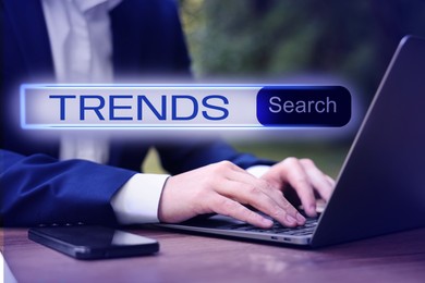 Image of Businessman using laptop to find hot tendencies, new ideas, popular directions at table, closeup. Search bar with word Trends