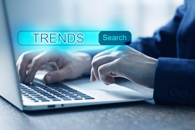 Image of Businessman using laptop to find hot tendencies, new ideas, popular directions at table, closeup. Search bar with word Trends
