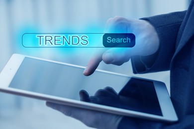 Image of Businessman using tablet computer to find hot tendencies, new ideas, popular directions, closeup. Search bar with word Trends