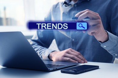 Image of Businessman using laptop and virtual screen to find hot tendencies, new ideas, popular directions at table, closeup. Search bar with word Trends