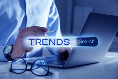 Image of Businessman using laptop and virtual screen to find hot tendencies, new ideas, popular directions at table, closeup. Search bar with word Trends