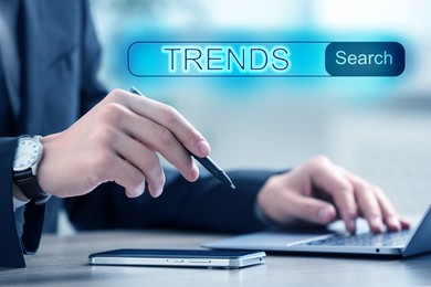 Image of Businessman using laptop to find hot tendencies, new ideas, popular directions at table, closeup. Search bar with word Trends