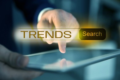 Image of Businessman using tablet computer to find hot tendencies, new ideas, popular directions, closeup. Search bar with word Trends
