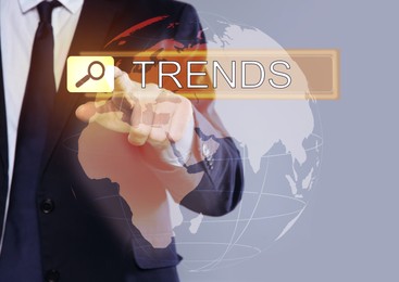 Image of Businessman using virtual screen to find hot tendencies, new ideas, popular directions against grey background, closeup. Search bar with word Trends and globe