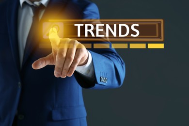 Image of Businessman using virtual screen to find hot tendencies, new ideas, popular directions against grey background, closeup. Search bar with word Trends