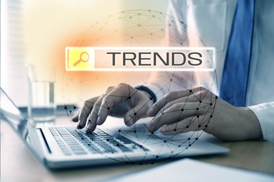 Image of Businessman using laptop to find hot tendencies, new ideas, popular directions at table, closeup. Search bar with word Trends and globe