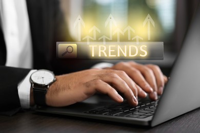Image of Businessman using laptop to find hot tendencies, new ideas, popular directions at table, closeup. Search bar with word Trends and arrows