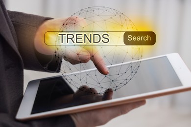 Image of Businessman using tablet computer to find hot tendencies, new ideas, popular directions, closeup. Search bar with word Trends