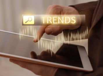 Image of Businessman using tablet computer to find hot tendencies, new ideas, popular directions, closeup. Search bar with word Trends and graph