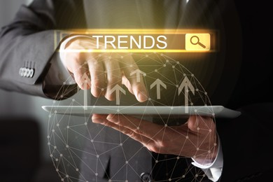 Image of Businessman using tablet computer to find hot tendencies, new ideas, popular directions, closeup. Search bar with word Trends, arrows and globe
