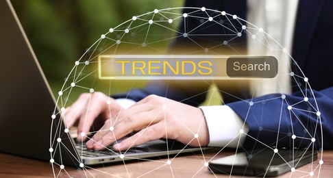 Image of Businessman using laptop to find hot tendencies, new ideas, popular directions at table, closeup. Search bar with word Trends and globe