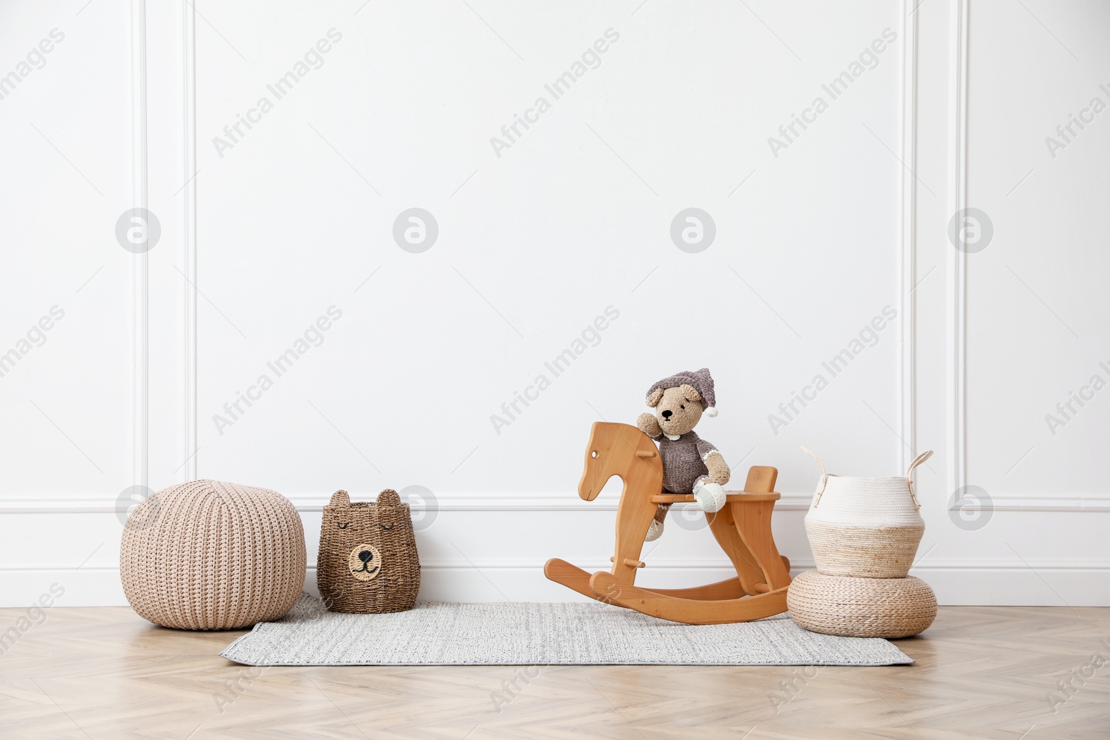 Rocking horse with bear toy, pouf and wicker baskets near white wall in child room. Interior design Photo of Rocking horse with bear toy, pouf and wicker baskets near white wall in child room. Interior design