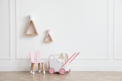 Photo of Child's toys, chair and wigwam shaped shelves on white wall indoors. Interior design
