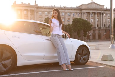 Photo of Beautiful woman with smartphone near modern car outdoors on sunny day