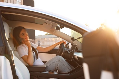 Photo of Woman talking on smartphone behind steering wheel of modern car, view from outside