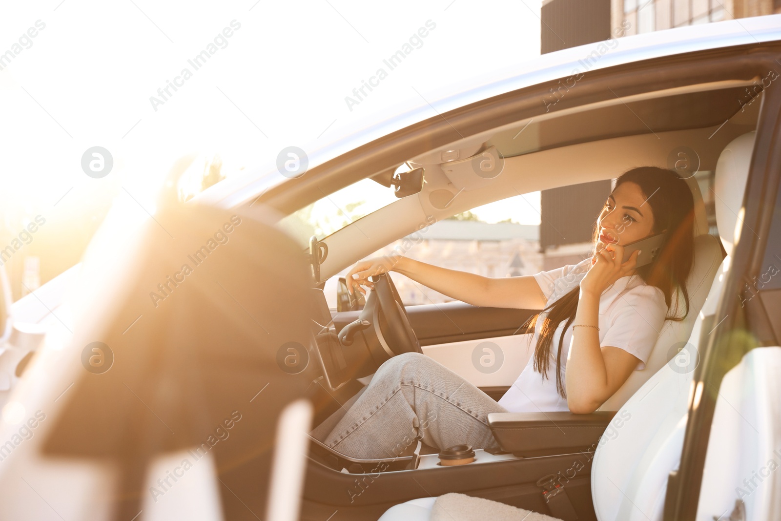 Photo of Woman talking on smartphone behind steering wheel of modern car, view from outside