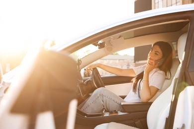 Photo of Woman talking on smartphone behind steering wheel of modern car, view from outside
