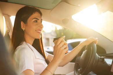 Photo of Woman with coffee behind steering wheel of modern car