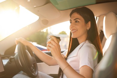 Photo of Woman with coffee behind steering wheel of modern car