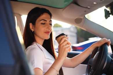 Photo of Woman with coffee behind steering wheel of modern car