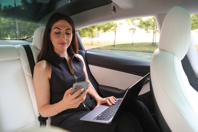 Photo of Woman with smartphone and laptop in modern car
