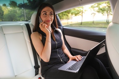 Photo of Woman with laptop talking on smartphone in modern car